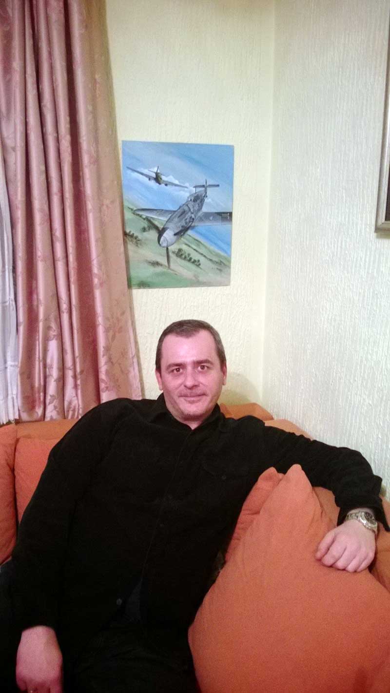 Дуле седи у свом стану, изнад њега уметничка слика коју је добио од мене на поклон. Две његове омиљене теме, немачки ловац Месершмит 109 у пилот Ерих Хартман.